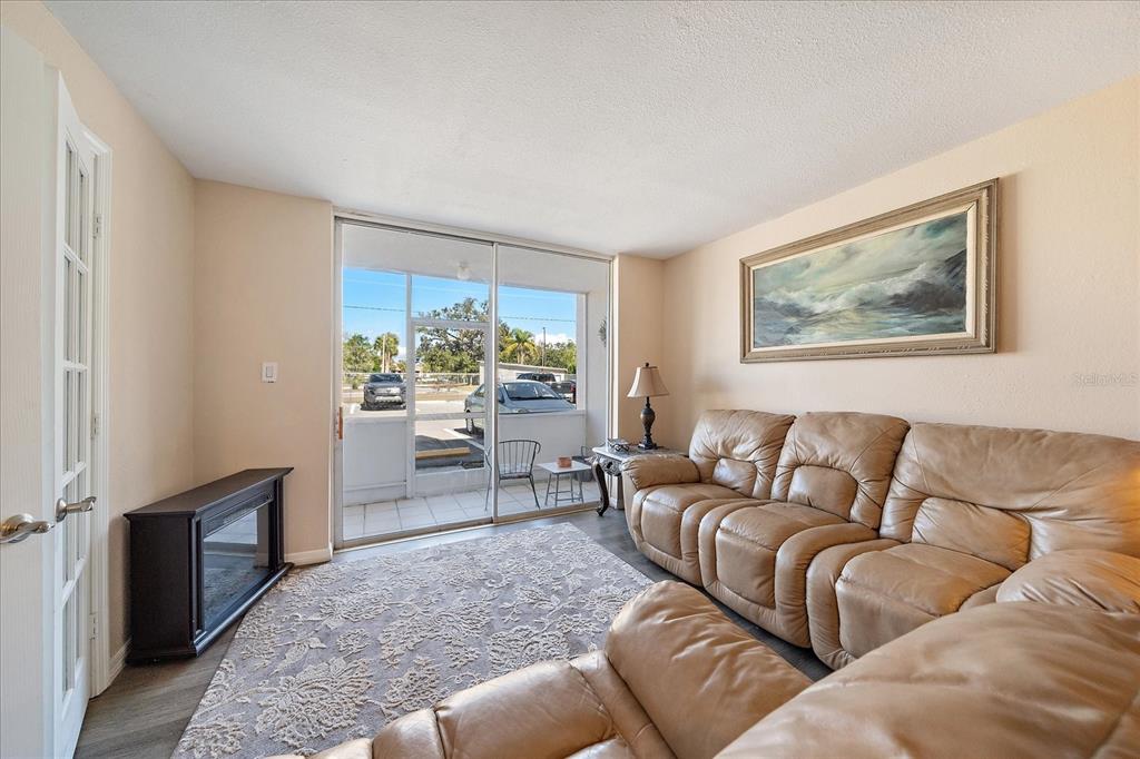A living room features a tan leather sofa, a patterned rug, and a sliding glass door — 519 ALBEE FARM ROAD UNIT 111, VENICE, FL