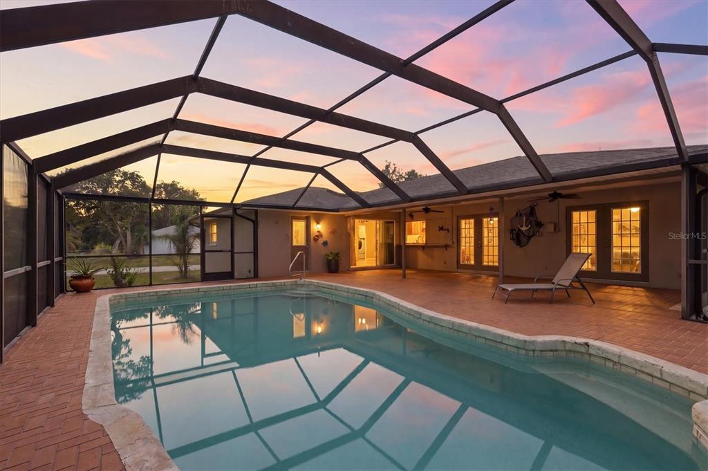 A screened-in patio features a swimming pool, brick pavers, and a view of the sunset — 1114 DEWHURST STREET, PORT CHARLOTTE, FL