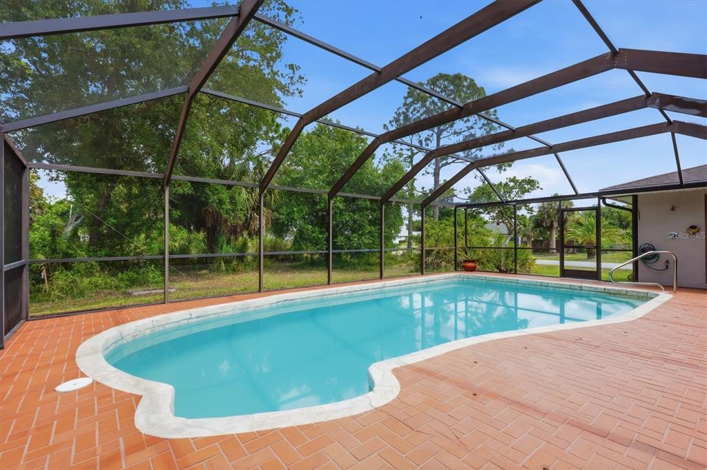 A screened-in swimming pool with a brick paver deck and surrounding trees — 1114 DEWHURST STREET, PORT CHARLOTTE, FL