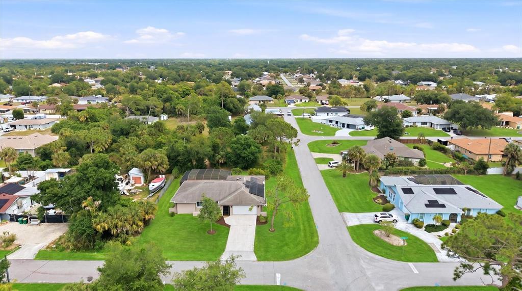 An aerial view shows suburban houses with green lawns and trees along a paved road — 1114 DEWHURST STREET, PORT CHARLOTTE, FL