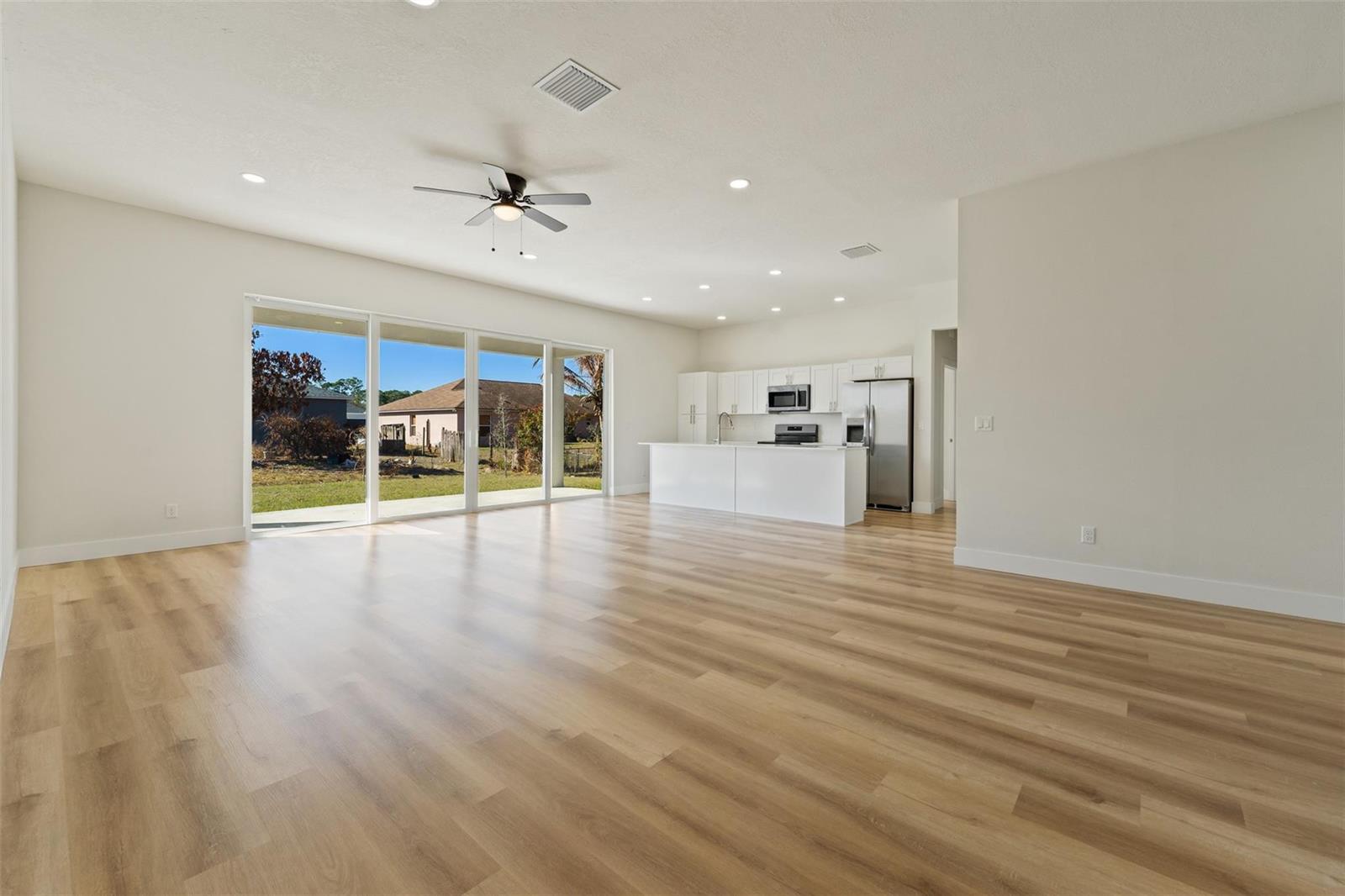An open-concept living area features light wood flooring, a kitchen with white cabinets, and sliding doors — 774 Cleaves Street, Palm Bay FL 32909, PALM BAY, FL