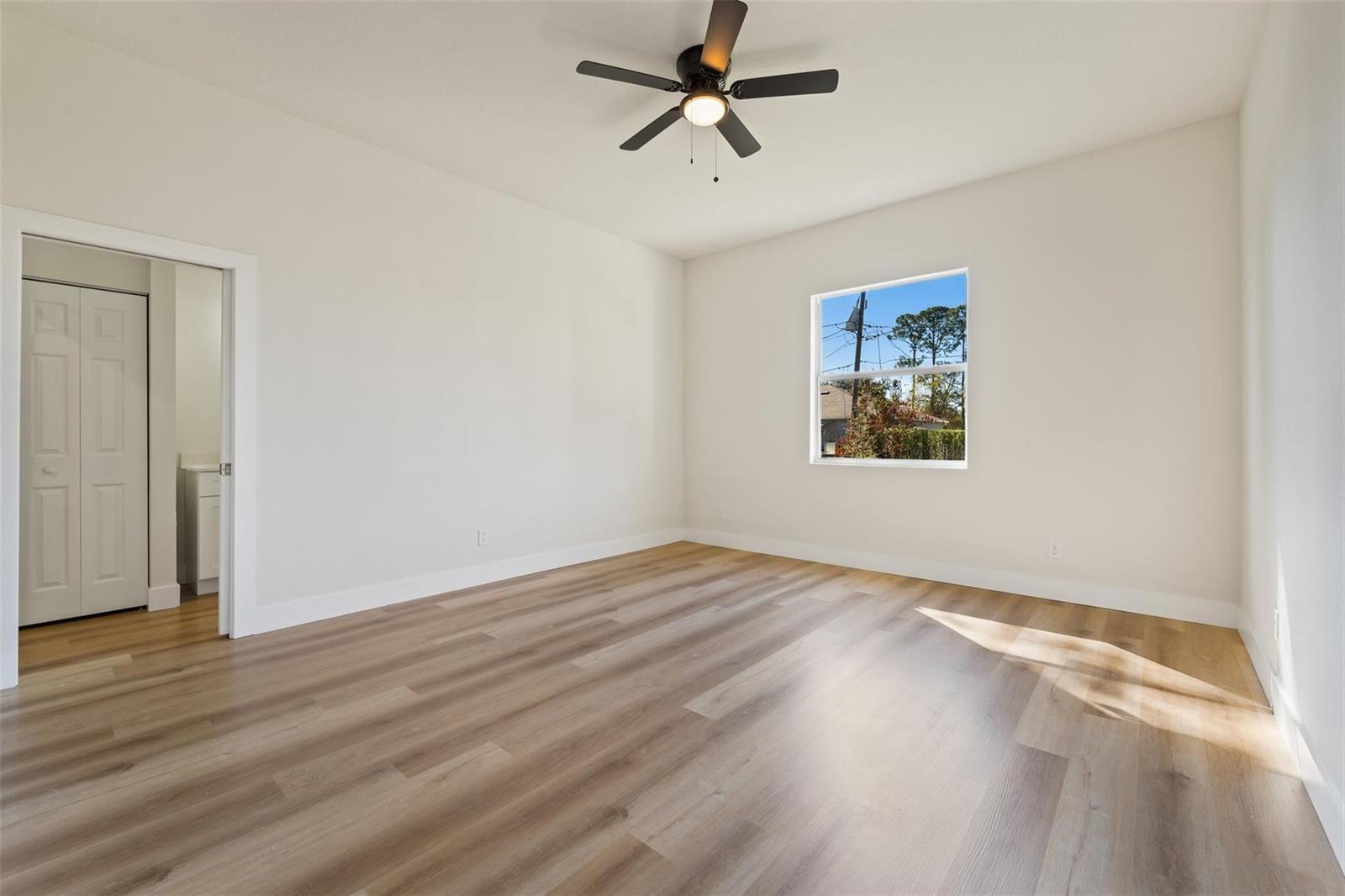 An empty bedroom features light wood-look flooring, white walls, a ceiling fan, and a window — 774 Cleaves Street, Palm Bay FL 32909, PALM BAY, FL