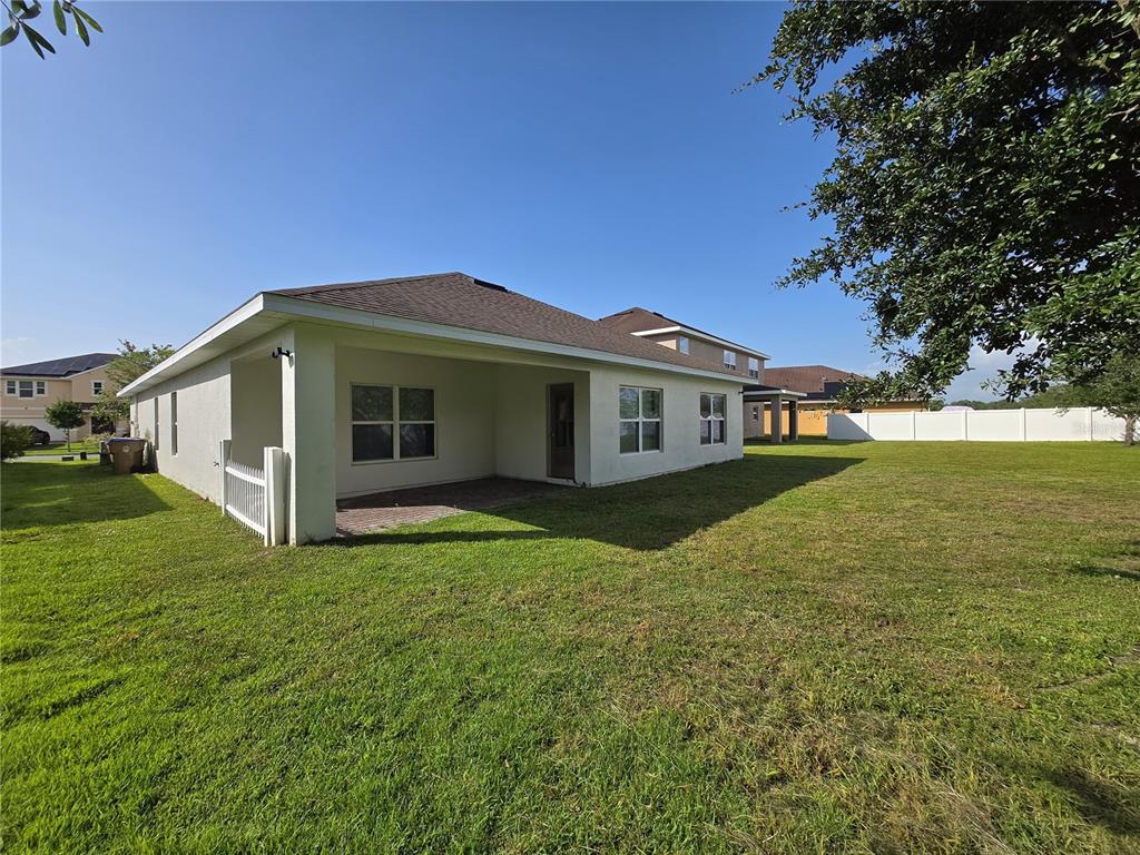The exterior rear view of a single-story house features a covered patio and lawn — 2476 ADDISON CREEK DRIVE, KISSIMMEE, FL
