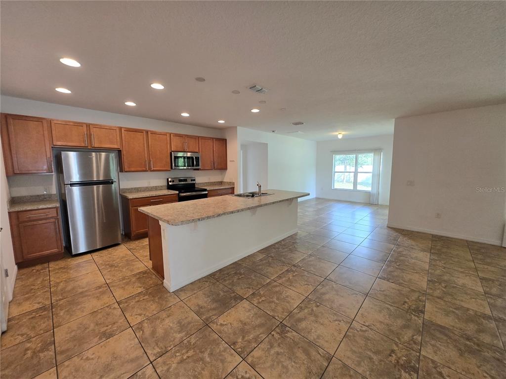 A kitchen with wood cabinets, stainless steel appliances, and a large island on tiled floors — 2476 ADDISON CREEK DRIVE, KISSIMMEE, FL