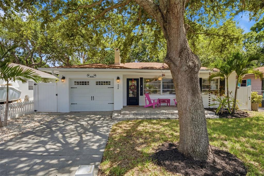 A white single-story house features a front-facing garage, a paved walkway, and a large tree — 1023 GRANADA STREET, CLEARWATER, FL