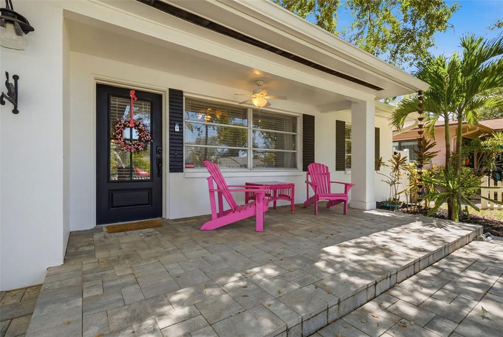 A front porch features two pink Adirondack chairs, a small table, and a black door — 1023 GRANADA STREET, CLEARWATER, FL