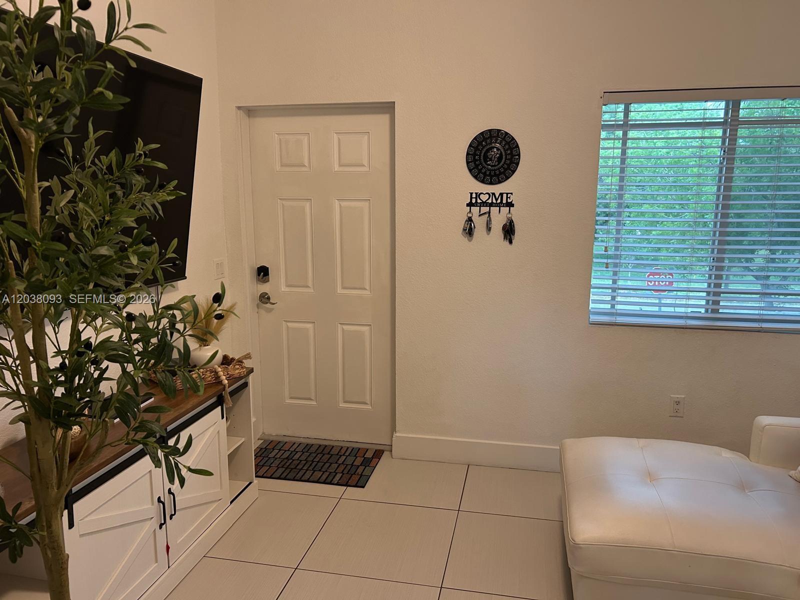 A room features a white door, a television, a potted plant, and a white ottoman — 106 SE 9th Ct # 201, Hallandale Beach FL 33009, HALLANDALE BEACH, FL