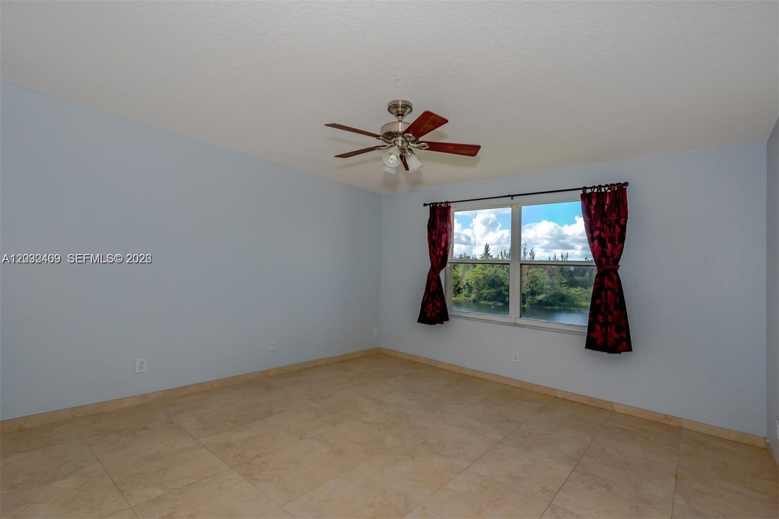 An empty bedroom features light blue walls, tile flooring, a ceiling fan, and a window — MIRAMAR, FL