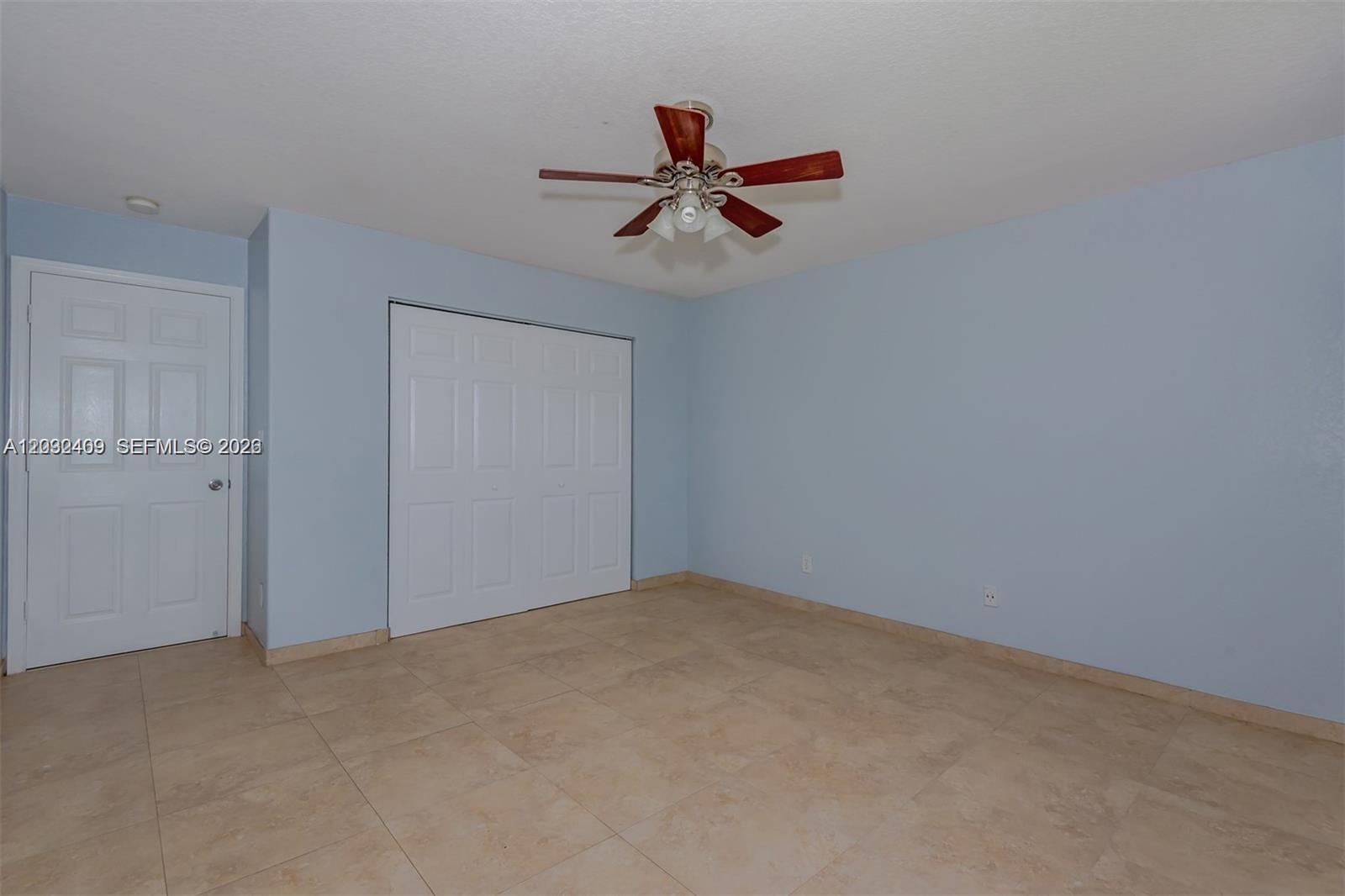 An empty bedroom features light blue walls, beige tile flooring, and a ceiling fan — MIRAMAR, FL