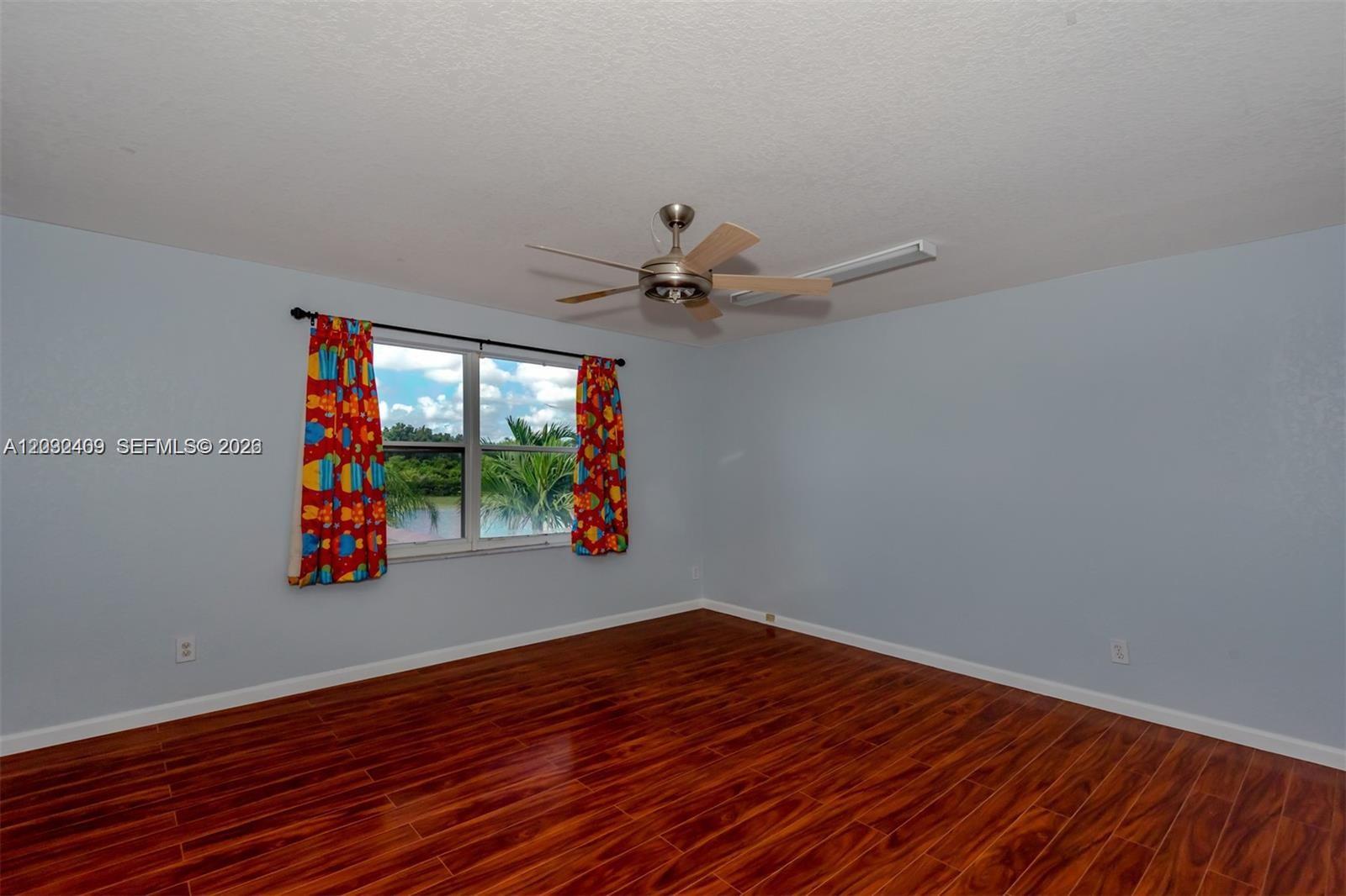 An empty bedroom features light blue walls, dark wood flooring, and a ceiling fan — MIRAMAR, FL