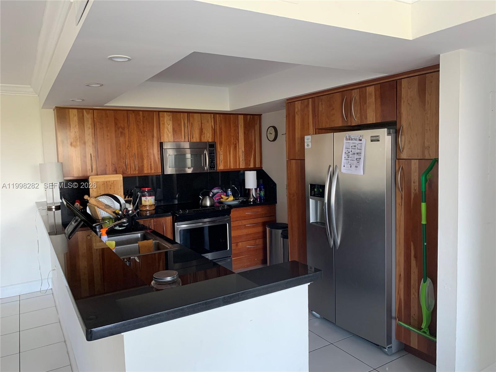 A kitchen features wood cabinets, black countertops, stainless steel appliances, and white tile flooring — 177 Ocean Lane Dr # 512, Key Biscayne FL 33149, KEY BISCAYNE, FL