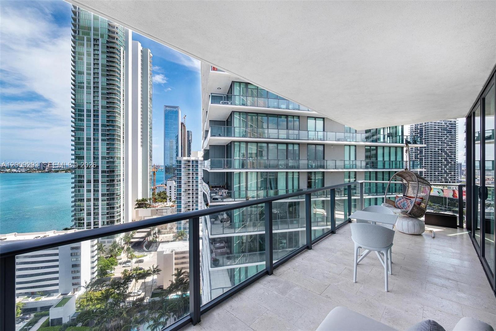 A high-rise balcony features a glass railing, outdoor seating, and views of nearby skyscrapers and water — 650 NE 32nd St # 2101, Miami FL 33137, MIAMI, FL