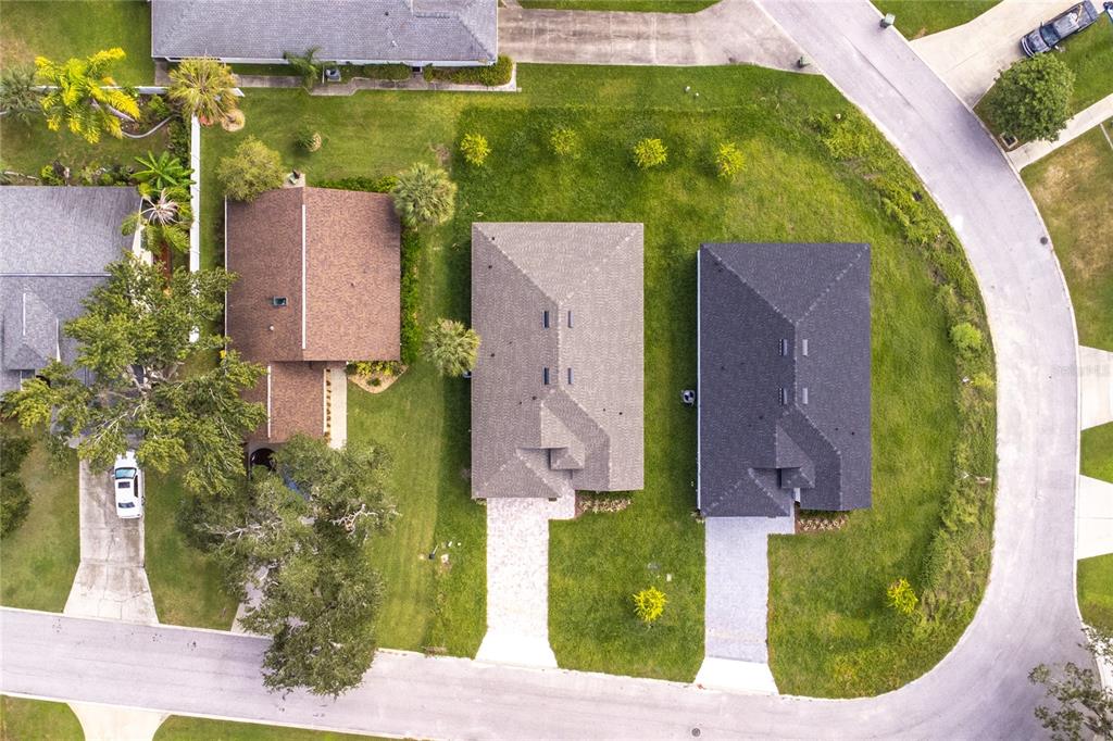 An aerial view shows three suburban houses with driveways and lawns along a curved street — 947 BELLE OAK DRIVE, LEESBURG, FL
