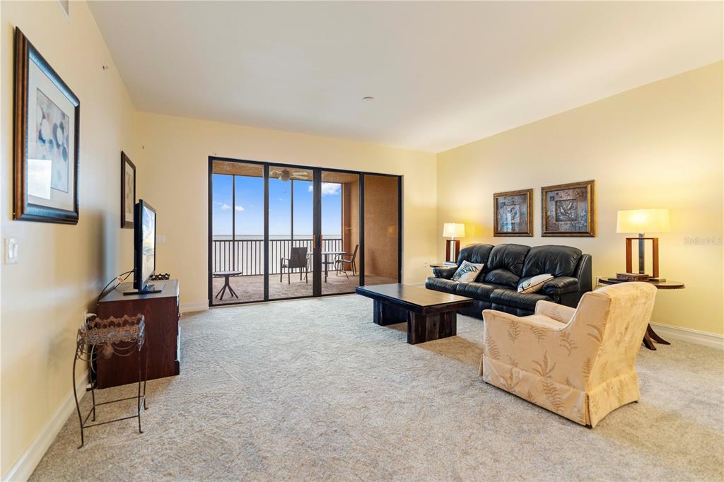 A living room features beige carpet, a black leather sofa, a patterned armchair, and a balcony — 85 VIVANTE BOULEVARD UNIT 8542, PUNTA GORDA, FL