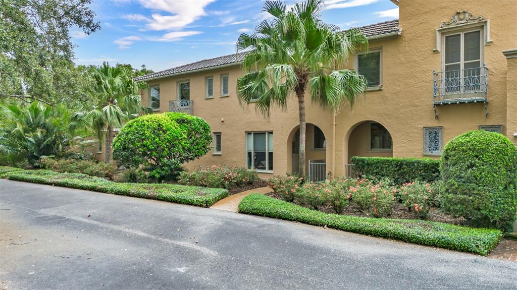 A two-story tan stucco building features arched entryways, a small balcony, and landscaped front gardens — 2300 N SCENIC HIGHWAY UNIT 37E, LAKE WALES, FL