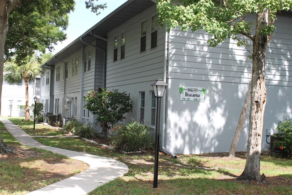 The exterior of a two-story gray apartment building with a sidewalk and landscaping — 10800 US HIGHWAY 19 N UNIT 220, PINELLAS PARK, FL