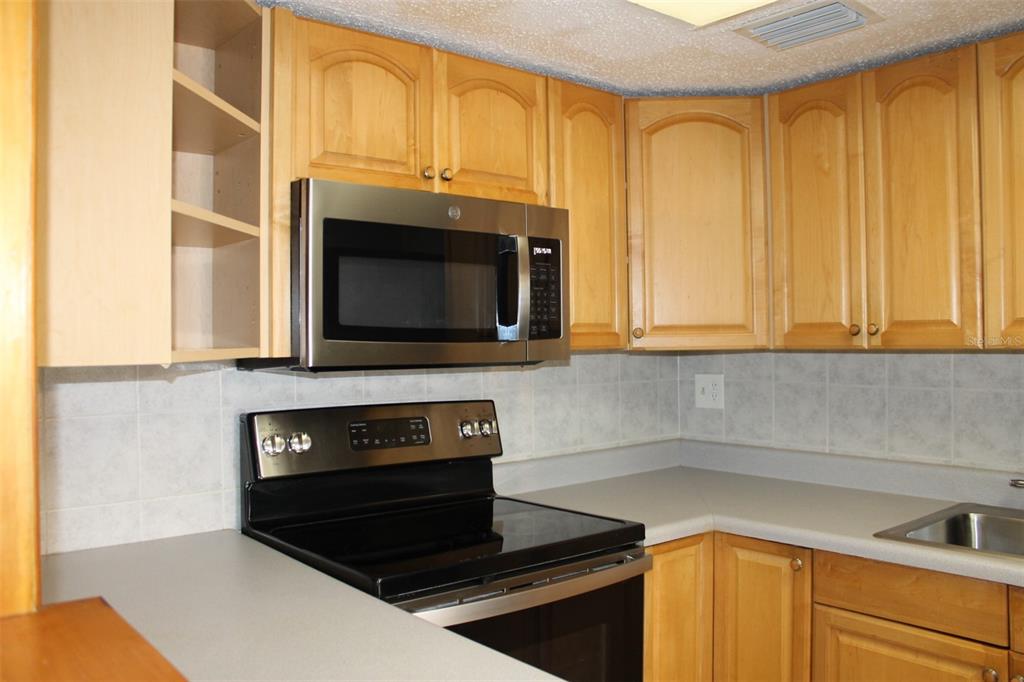 A kitchen features light wood cabinets, stainless steel appliances, and a gray countertop — 10800 US HIGHWAY 19 N UNIT 220, PINELLAS PARK, FL