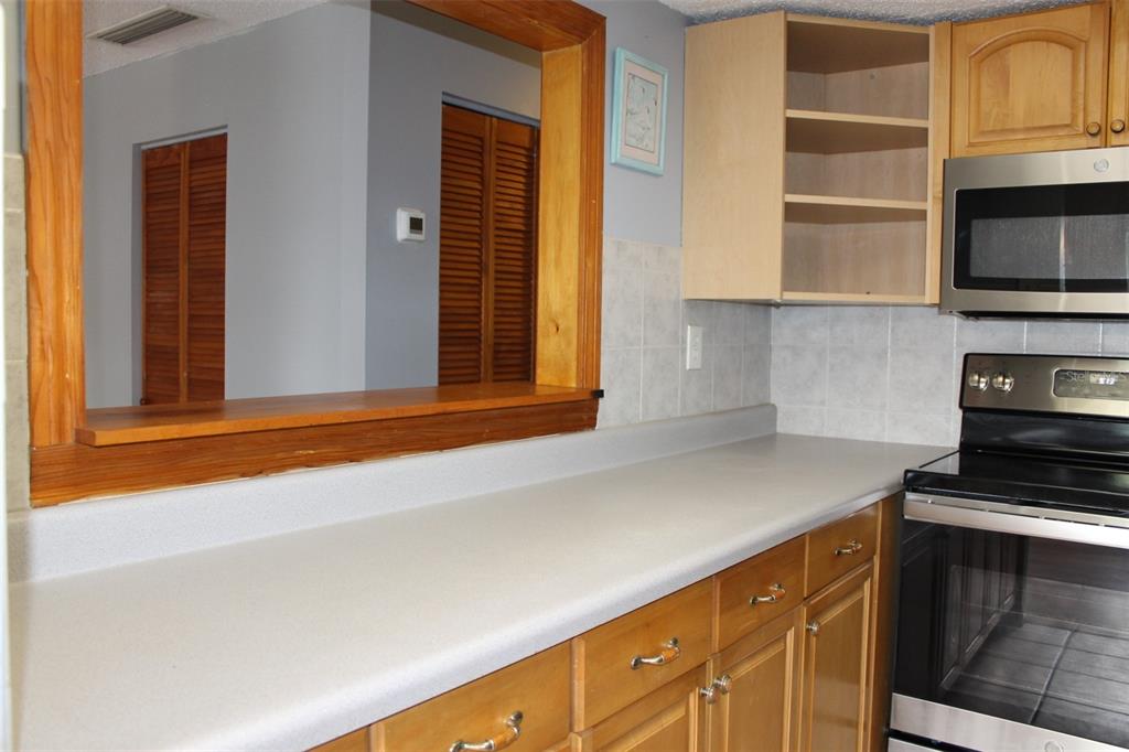 A kitchen features wooden cabinets, a gray countertop, a stainless steel stove, and a pass-through window — 10800 US HIGHWAY 19 N UNIT 220, PINELLAS PARK, FL