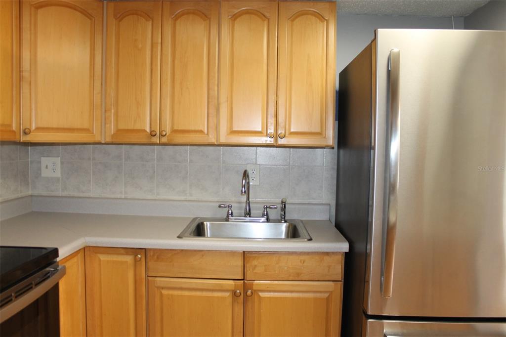 A kitchen features light wood cabinets, a stainless steel sink, and a stainless steel refrigerator — 10800 US HIGHWAY 19 N UNIT 220, PINELLAS PARK, FL
