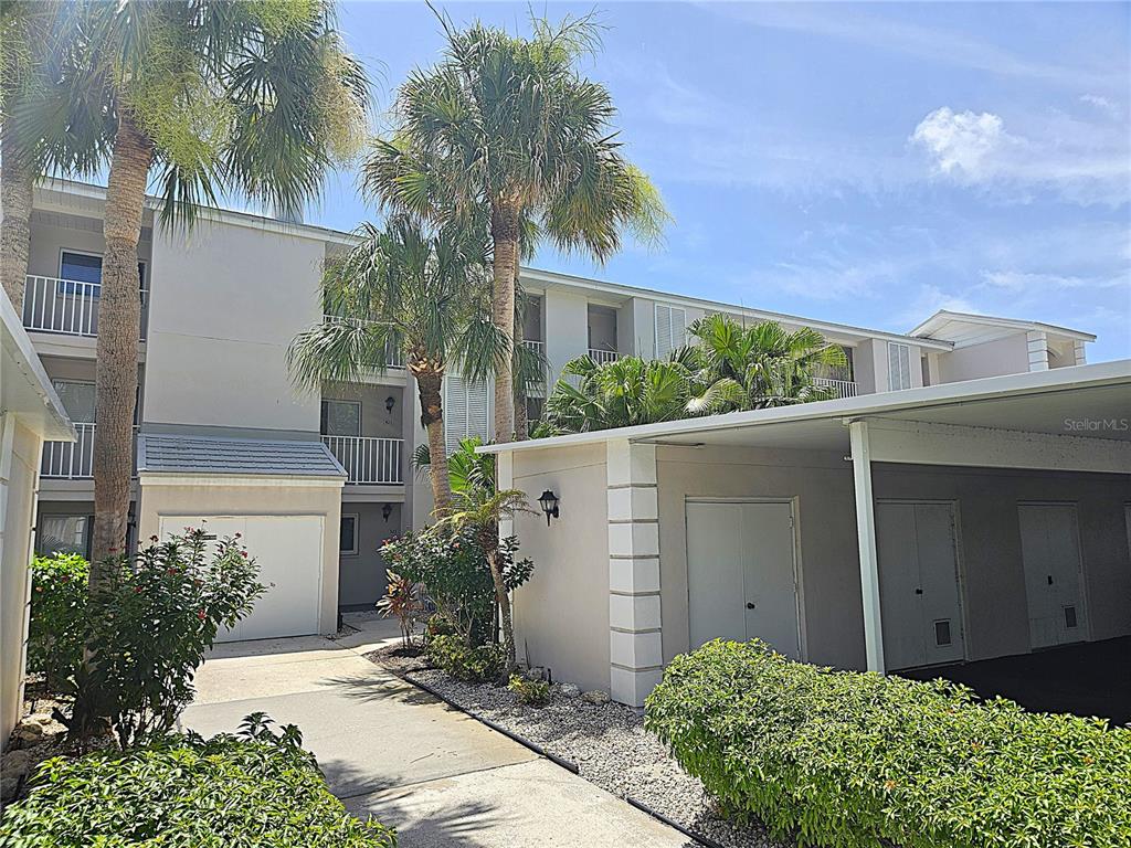 A multi-story apartment building features a covered parking area and palm trees in the foreground — 437 CERROMAR LANE UNIT 424, VENICE, FL
