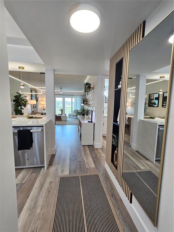 A hallway with wood-slat wall paneling and a large mirror leads to an open-concept kitchen — 437 CERROMAR LANE UNIT 424, VENICE, FL