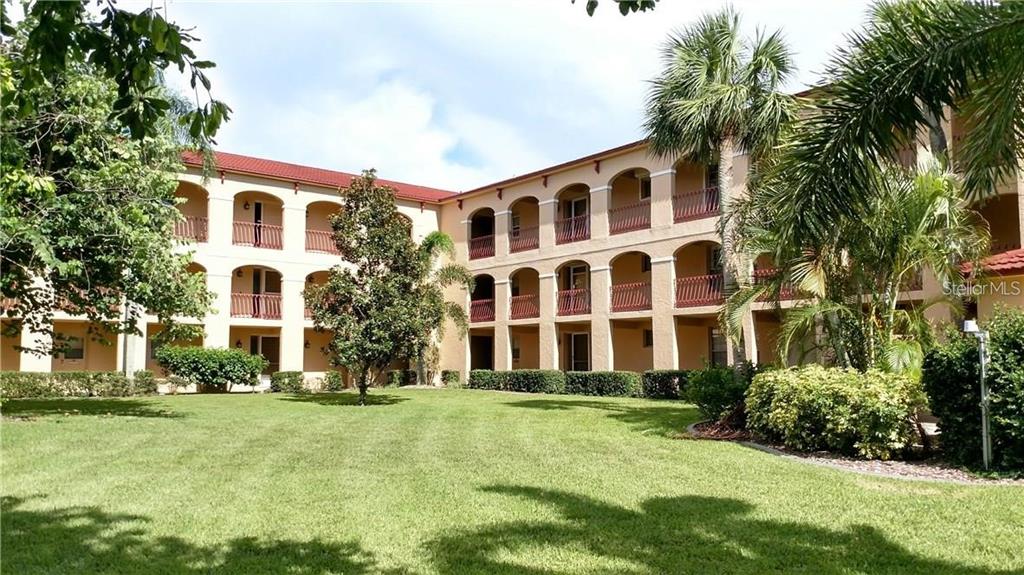 A three-story apartment building with arched balconies overlooks a grassy lawn and palm trees — 1 COLONY POINT DRIVE UNIT A5, PUNTA GORDA, FL