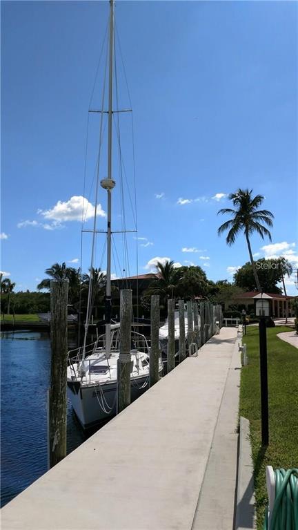 A sailboat is docked at a concrete pier next to a palm tree and canal — 1 COLONY POINT DRIVE UNIT A5, PUNTA GORDA, FL