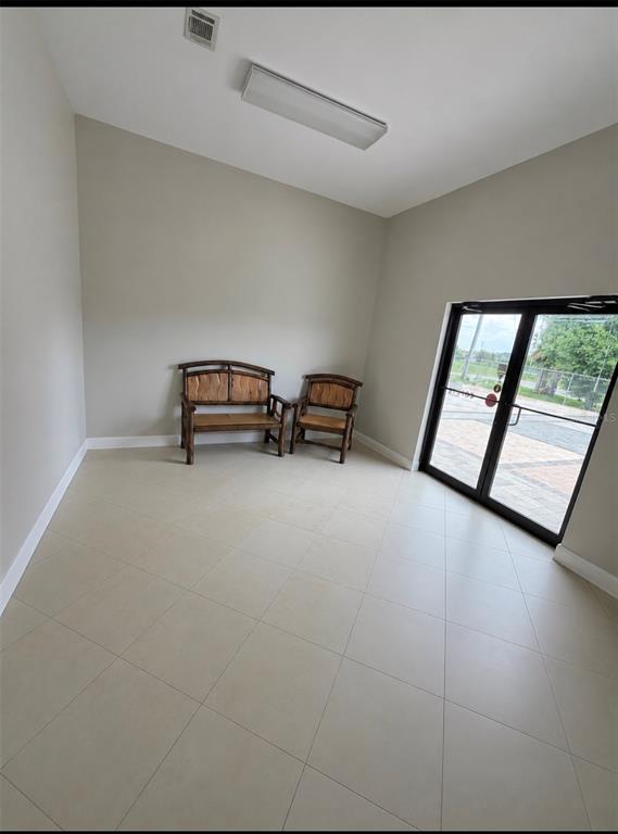 A room with light-colored tile flooring, beige walls, two wooden chairs, and a glass door — 1730 S US HIGHWAY 27, CLERMONT, FL
