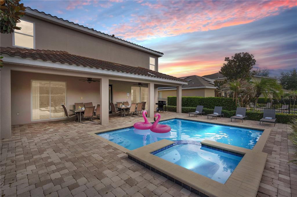A backyard patio features a swimming pool, a hot tub, and two pink flamingo floats — 7657 WILMINGTON LOOP, KISSIMMEE, FL