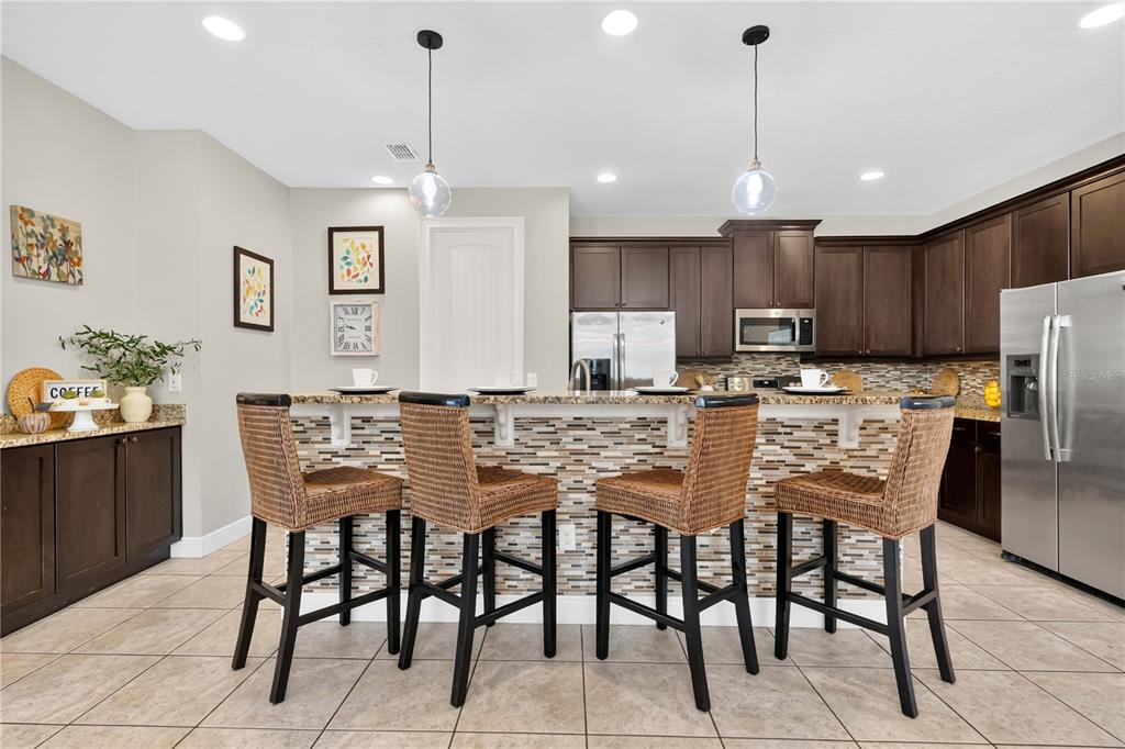 A kitchen features dark wood cabinets, a tiled breakfast bar, and four wicker bar stools — 7657 WILMINGTON LOOP, KISSIMMEE, FL
