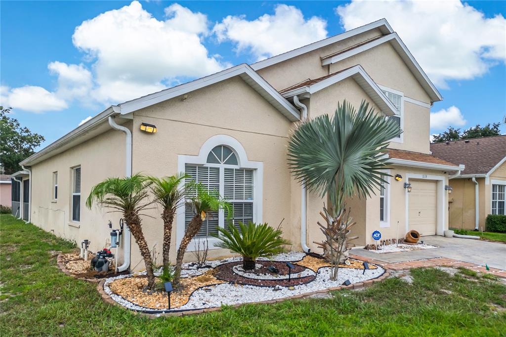 A two-story house with a tan stucco exterior, a small front yard, and a garage — 1228 SANDY RIDGE DRIVE, DAVENPORT, FL
