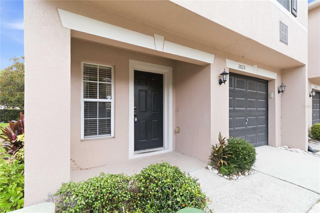 The exterior of a tan townhouse features a black front door and a garage — 2825 CLIFFE COURT, OVIEDO, FL