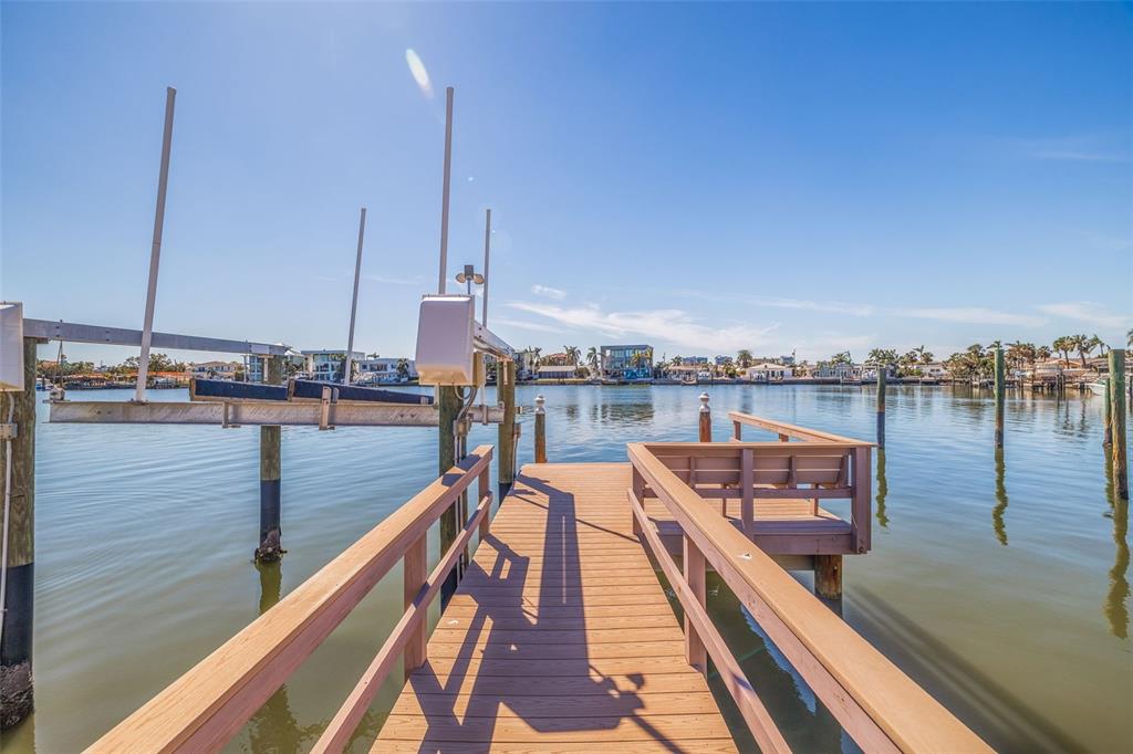 A wooden dock with a boat lift extends over calm water under a clear blue sky — 7874 9TH AVENUE S, ST PETERSBURG, FL