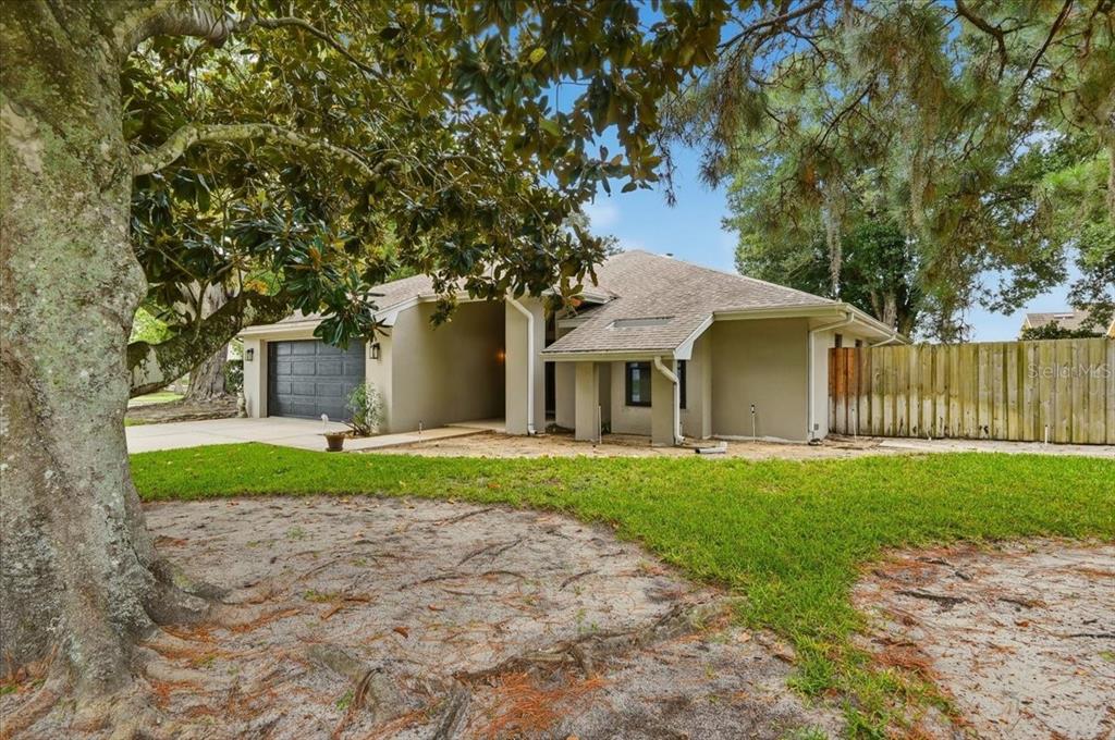 A single-story house with a gray garage, tan exterior, and a large tree in front — 238 COLLEGE GROVE CIRCLE NE, WINTER HAVEN, FL