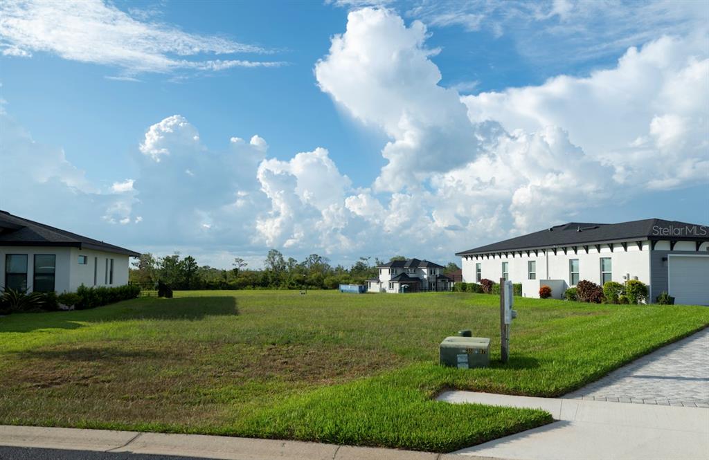 A vacant, grassy residential lot sits between two modern houses under a cloudy blue sky — 338 SPINNAKER COURT, AUBURNDALE, FL