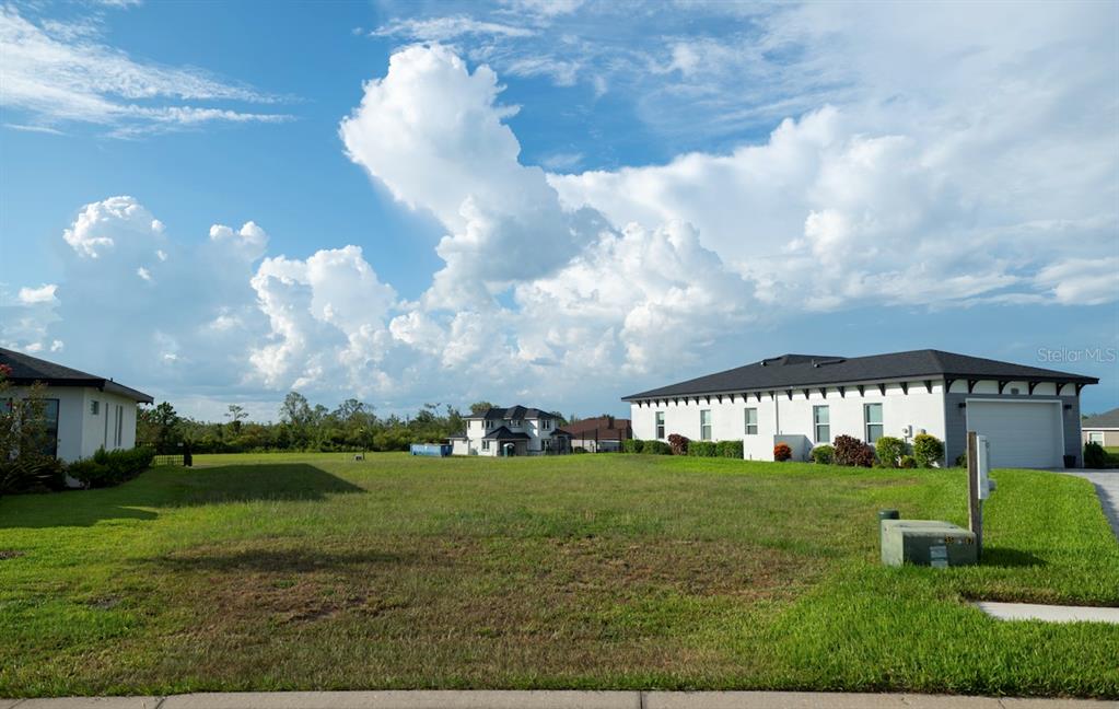 A vacant grassy residential lot sits between two modern houses under a cloudy blue sky — 338 SPINNAKER COURT, AUBURNDALE, FL