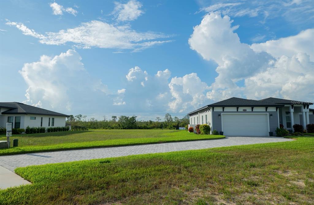 A paved driveway leads between two modern houses toward a grassy field under a cloudy sky — 338 SPINNAKER COURT, AUBURNDALE, FL