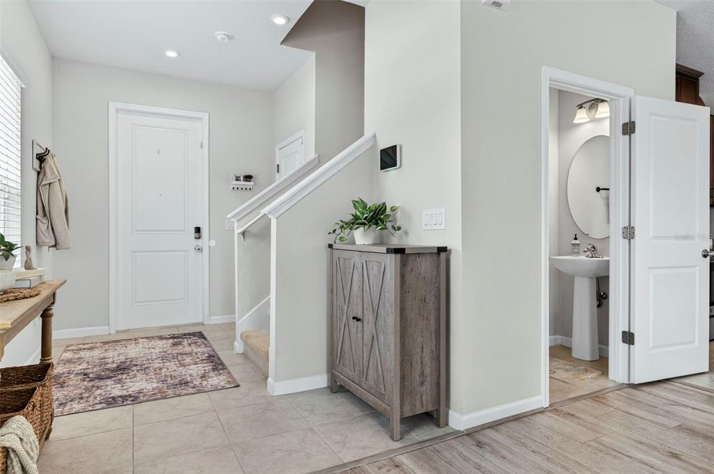 A bright entryway features tile flooring, a staircase, a wooden cabinet, and a powder room — 381 CRESTWIND DRIVE, DAYTONA BEACH, FL