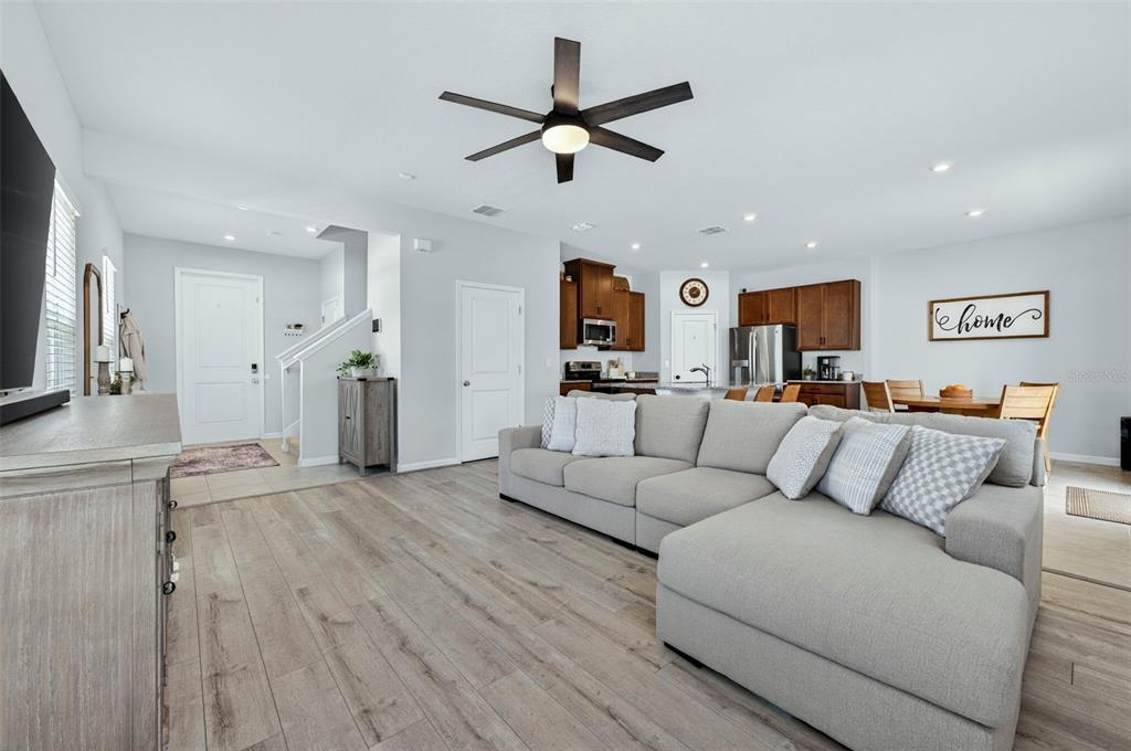 An open-concept living room features light wood flooring, a large gray sectional, and a kitchen — 381 CRESTWIND DRIVE, DAYTONA BEACH, FL