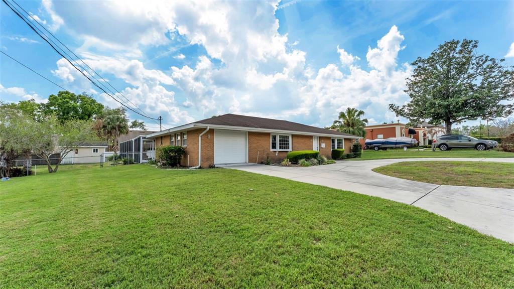 A single-story brick house with a garage and a large front lawn under a cloudy sky — 901 WOODWARD STREET, LAKELAND, FL