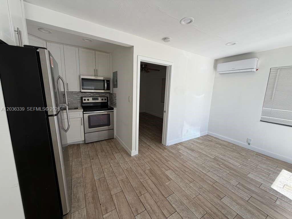 A kitchen with white cabinets and stainless steel appliances opens into a living area — 5843 Harding St, Hollywood FL 33021, HOLLYWOOD, FL