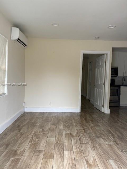 A room with light-colored walls, wood-look tile flooring, and a wall-mounted air conditioning unit — 5843 Harding St, Hollywood FL 33021, HOLLYWOOD, FL