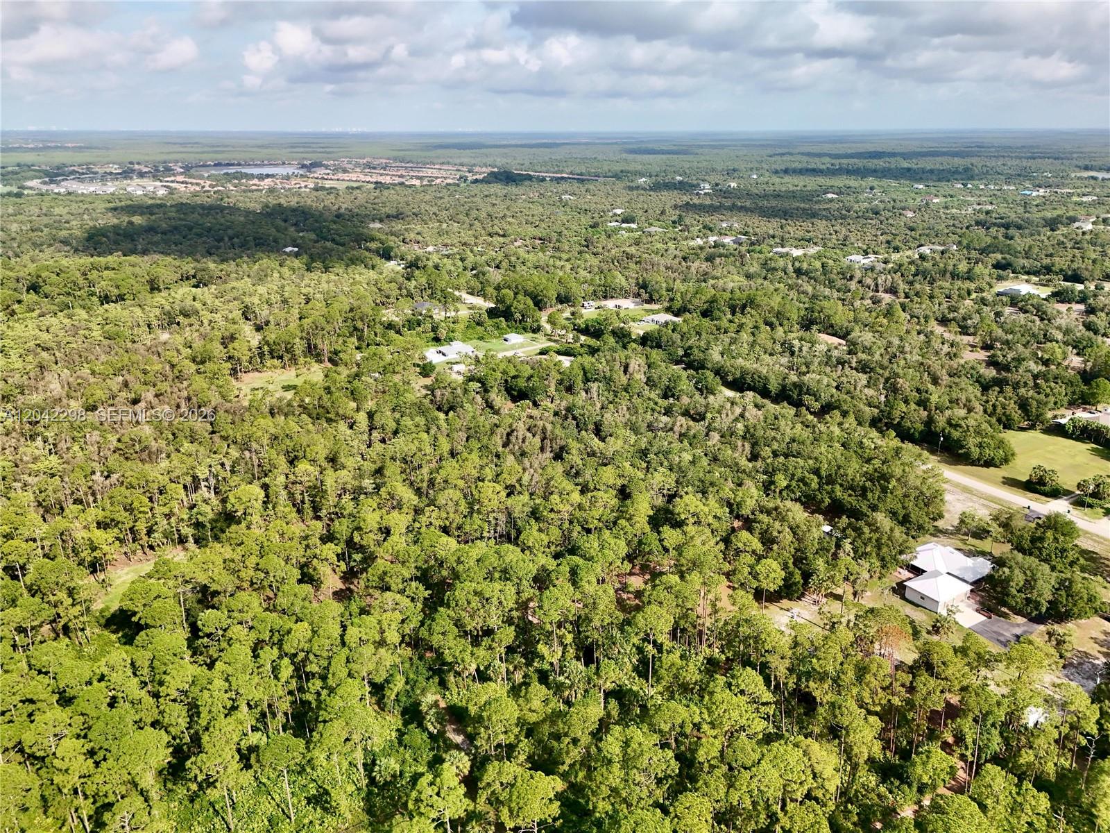 An aerial view shows a dense forest landscape with scattered houses and a paved road — 260 35TH AVE NW, Naples FL 34120, NAPLES, FL