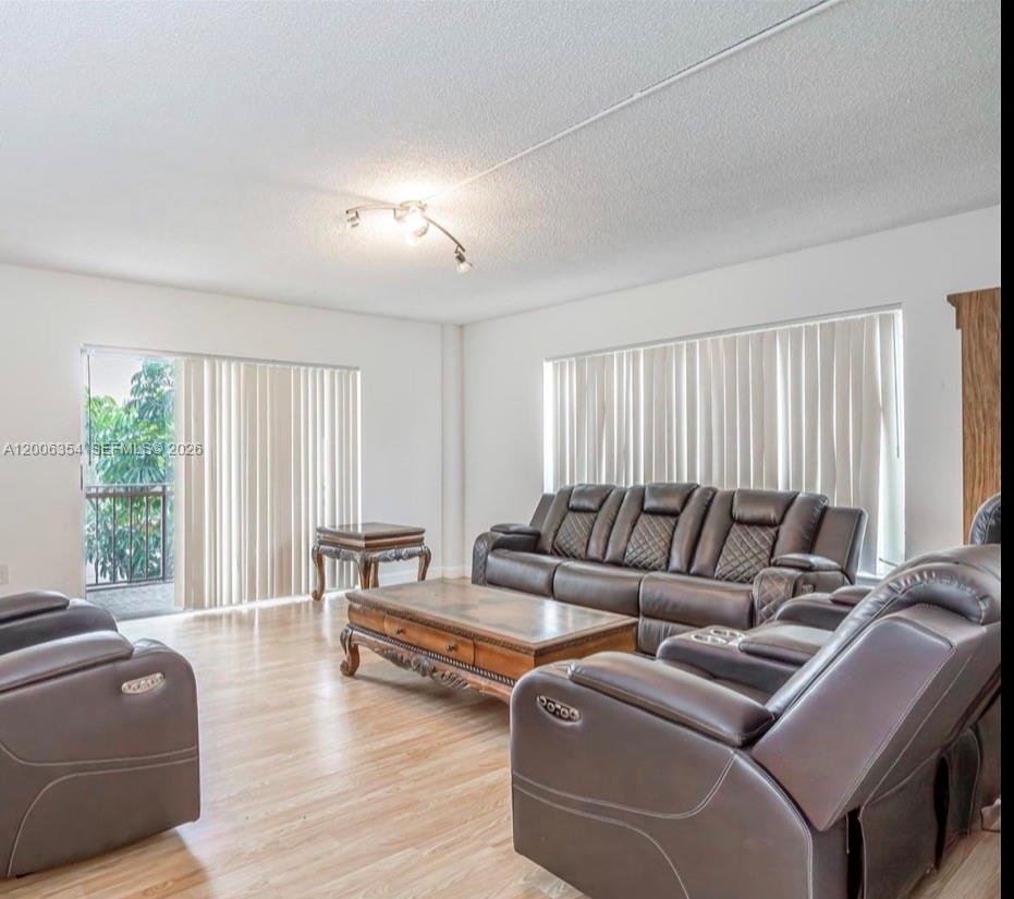 A living room features light wood flooring, dark leather furniture, and vertical window blinds — 4174 Inverrary Dr # 202, Lauderhill FL 33319, LAUDERHILL, FL