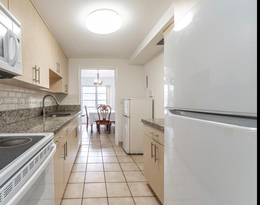 A galley kitchen features light wood cabinets, granite countertops, and white appliances — 4174 Inverrary Dr # 202, Lauderhill FL 33319, LAUDERHILL, FL
