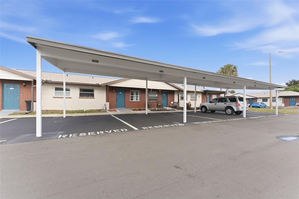 A covered parking structure sits in front of a single-story residential building with brick accents — 24862 US HIGHWAY 19 N UNIT 1604, CLEARWATER, FL