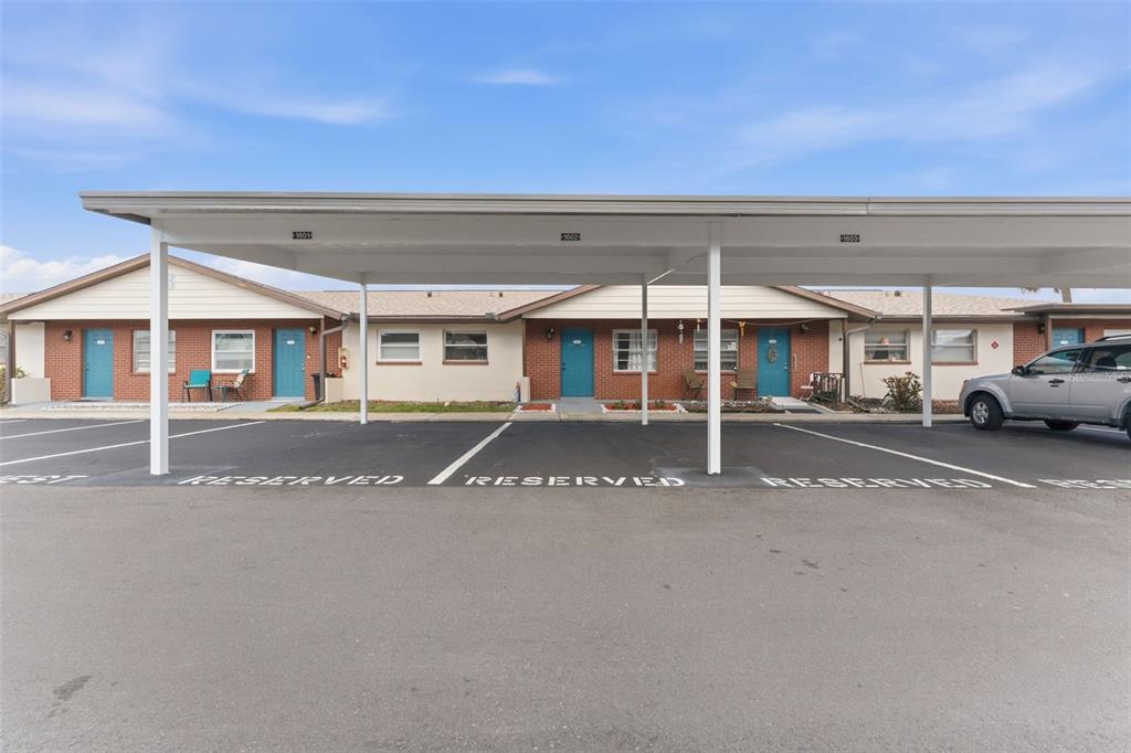 A row of single-story brick apartments with a covered parking structure in the foreground — 24862 US HIGHWAY 19 N UNIT 1604, CLEARWATER, FL