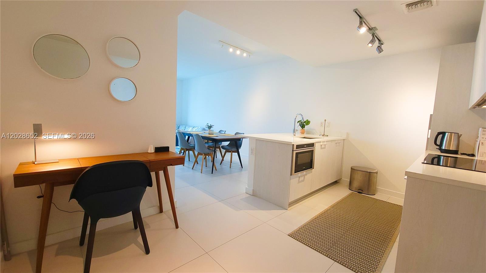 A modern kitchen with a white island and dining area is visible from a desk space — 501 NE 31st St # 1002, Miami FL 33137, MIAMI, FL