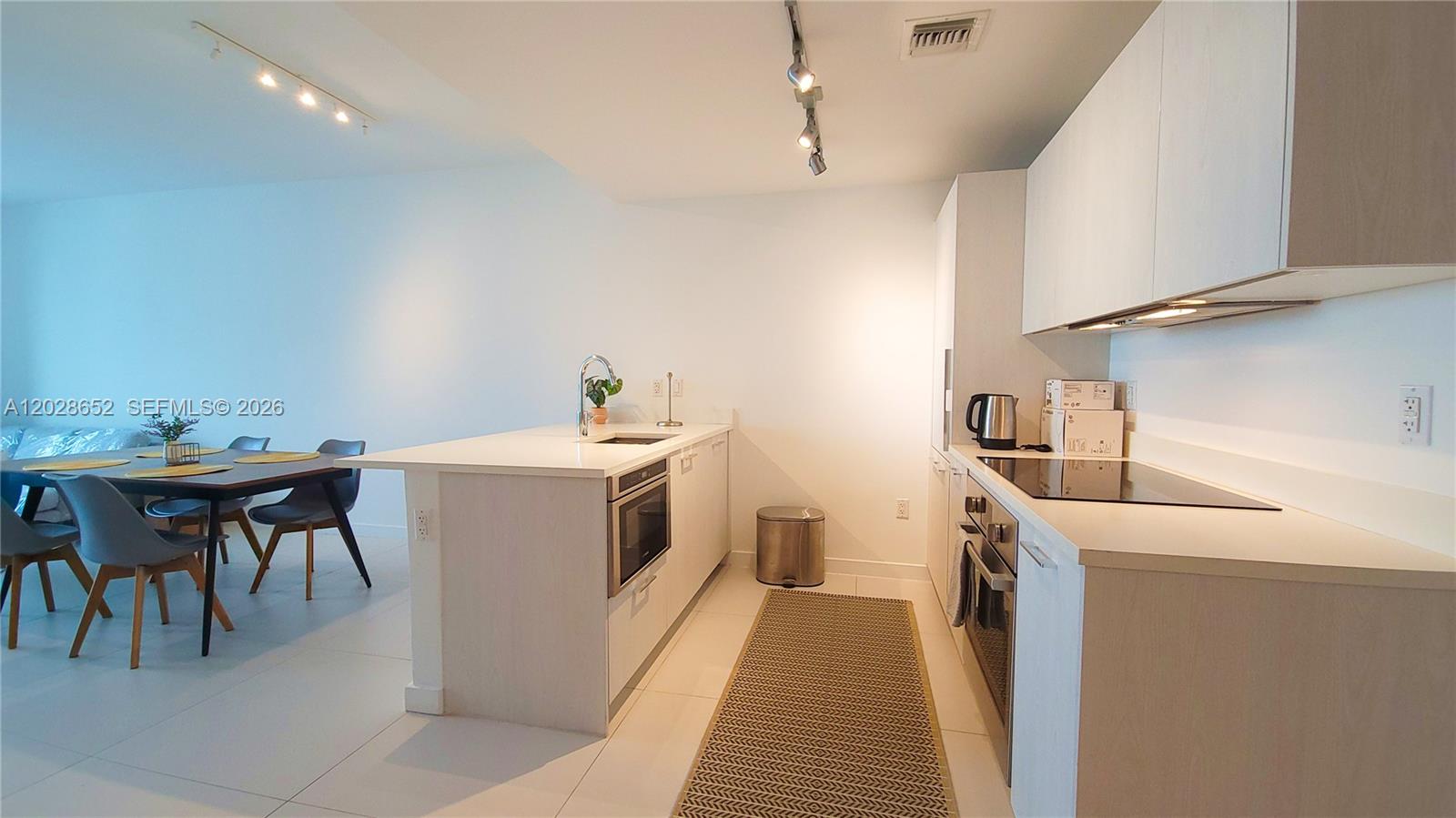 A modern kitchen features white cabinetry, light countertops, and a dining area with gray chairs — 501 NE 31st St # 1002, Miami FL 33137, MIAMI, FL