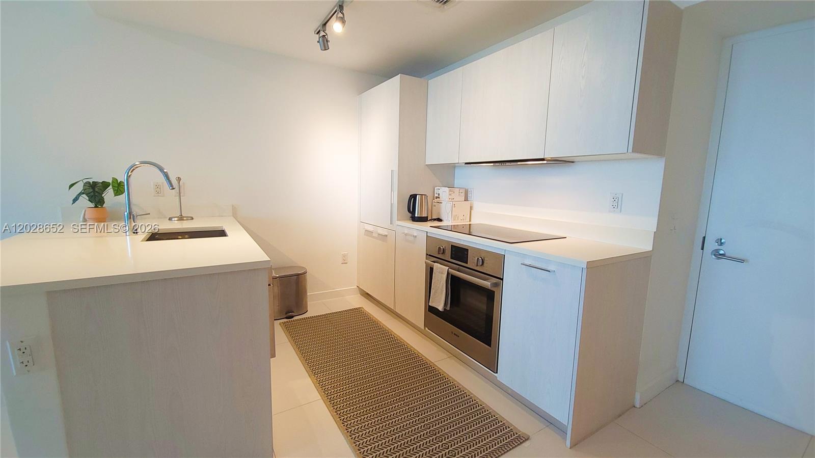 A modern kitchen features white cabinetry, stainless steel appliances, and a light-colored countertop — 501 NE 31st St # 1002, Miami FL 33137, MIAMI, FL